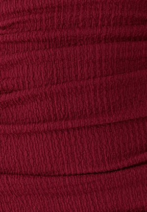 Nahaufnahme eines strukturierten, tiefroten Stoffes mit einem zerknitterten und elastischen Oberflächenmuster.