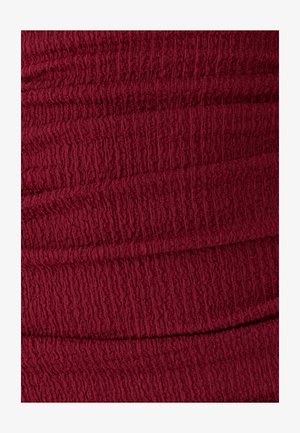 Nahaufnahme eines strukturierten, tiefroten Stoffes mit einem zerknitterten und elastischen Oberflächenmuster.