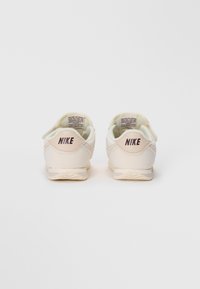Par bijelih Nike tenisica s bež detaljima, prikazanih s leđa, koje pokazuju Nike logo na peti i tekst na unutarnjem jeziku.