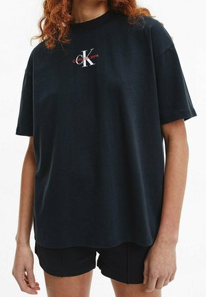 Černé bavlněné tričko s krátkými rukávy a kulatým výstřihem. Na hrudi má bílý a červený nápis "Calvin Klein Jeans".