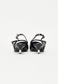 Crne lakirane kožne potpetice sa slingback dizajnom, s oštrim vrhom i metalnim detaljem na potpetici. Glatka tekstura, minimalistički stil.