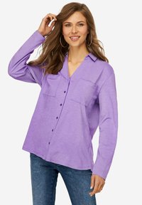 Camicia oversized lavanda con maniche lunghe, due tasche sul petto, chiusura davanti con bottoni e un tessuto morbido e strutturato. Abbinata a jeans in denim.