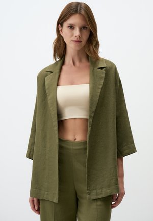 Olijfgroene linnen blazer met een losse pasvorm, reverskraag en driekwart mouwen, gecombineerd met een nude crop top en bijpassende broek.