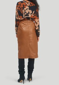 Kvinna i brun fusk läder midikjol, svart blommig blus och svarta högklackade knäkorta stövlar, sedd bakifrån.