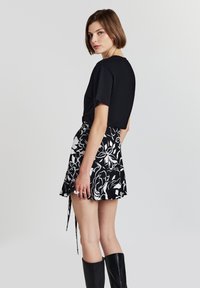 Top nero a maniche corte abbinato a una gonna a ruota floreale in bianco e nero. L'outfit presenta un delicato dettaglio a nodo e stivali neri fino al ginocchio.