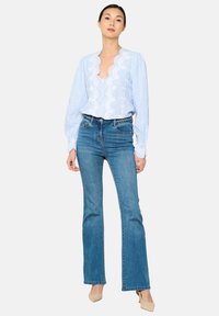 Blusa a rayas azul y blanca con escote en V y detalles bordados, combinada con jeans acampanados azul medio y tacones beige.