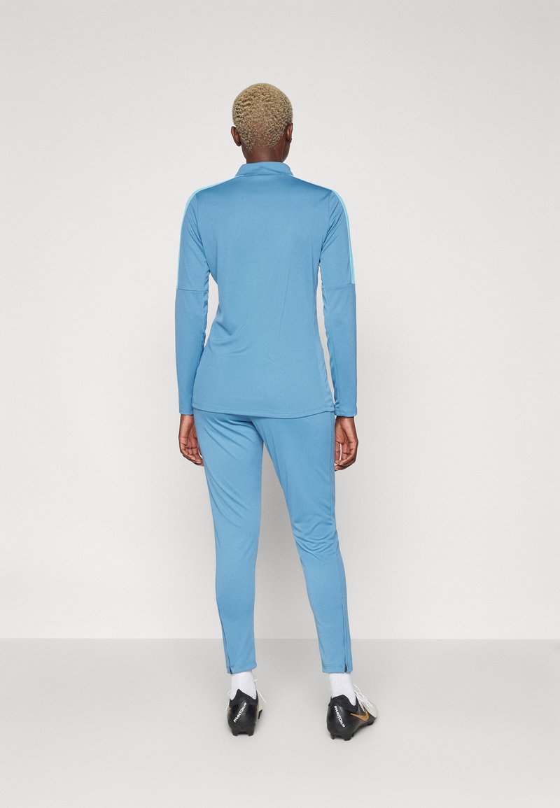 Hellblauer Sportanzug mit langen Ärmeln und Hosen, aus einem glatten Material gefertigt, mit einem Kragen und kontrastierenden Seitenakzenten.