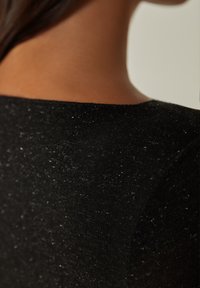 Sort tekstureret stof med en subtil glans, der har en glat overflade og en tætsiddende design ved halsudskæringen og skulderområdet.
