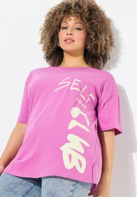 Camiseta rosa de manga corta en tela suave con "SELF LOVE CLUB" impreso en letras blancas grandes, con un corte relajado y aberturas en los lados.