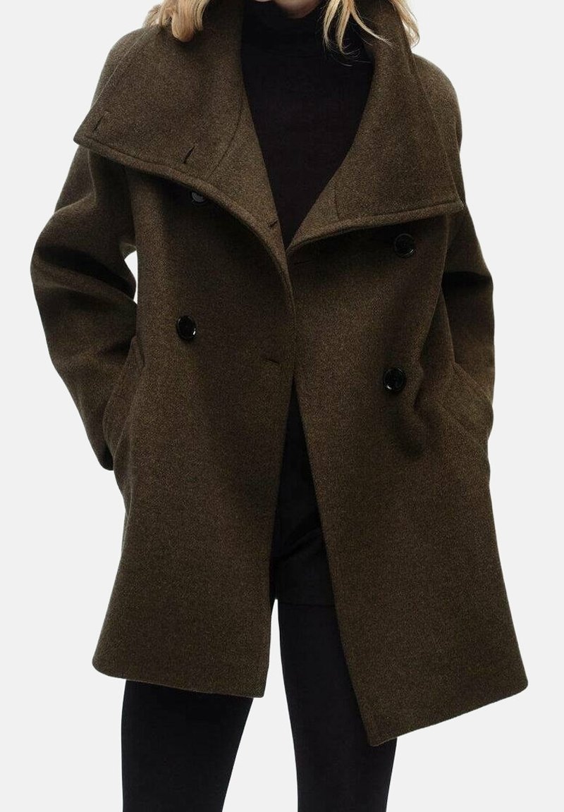 Femme portant un manteau en laine vert olive foncé à double boutonnage, col large, les mains dans les poches, associé à un col roulé noir et un pantalon.