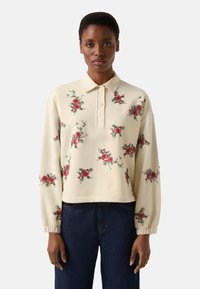 Kremowy sweter z kwiatowym haftem w czerwieni i zieleni, z kołnierzem, zapięciem na guziki i marszczonymi rękawami.