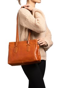 Bruine lederen tote bag met twee lange handvatten, rechthoekige vorm, zichtbare stikdetails en een gladde textuur.