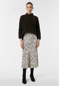 Ciemnobrązowy sweter z dzianiny z wysokim kołnierzem, w zestawieniu z midi spódnicą w kremowo-czarny wzór oraz czarnymi botkami za kostkę.