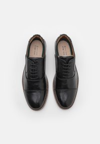 Chaussures en cuir noir avec un bout arrondi, un laçage, une texture lisse et une couture contrastante le long de la semelle. La semelle intérieure est beige.