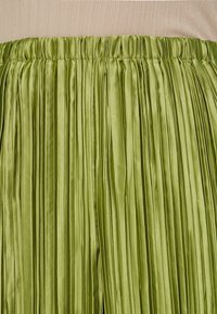 Spódnica plisowana z jasnej zielonej satyny, z pionowymi zakładkami i elastycznym pasem. Materiał ma gładką, błyszczącą fakturę.