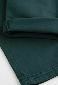 Ciemnozielony materiał o gładkiej fakturze, z podwiniętym wykończeniem i subtelnym diagonalnym wzorem w tkaninie. Zbliżenie na szczegóły materiału.