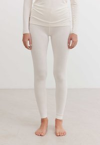 Fehér, testhezálló leggings puha, rugalmas anyagból. Sima felület ribbed derékpánttal és szoros mandzsettákkal a bokákon. Meztelen lábfejek láthatók.