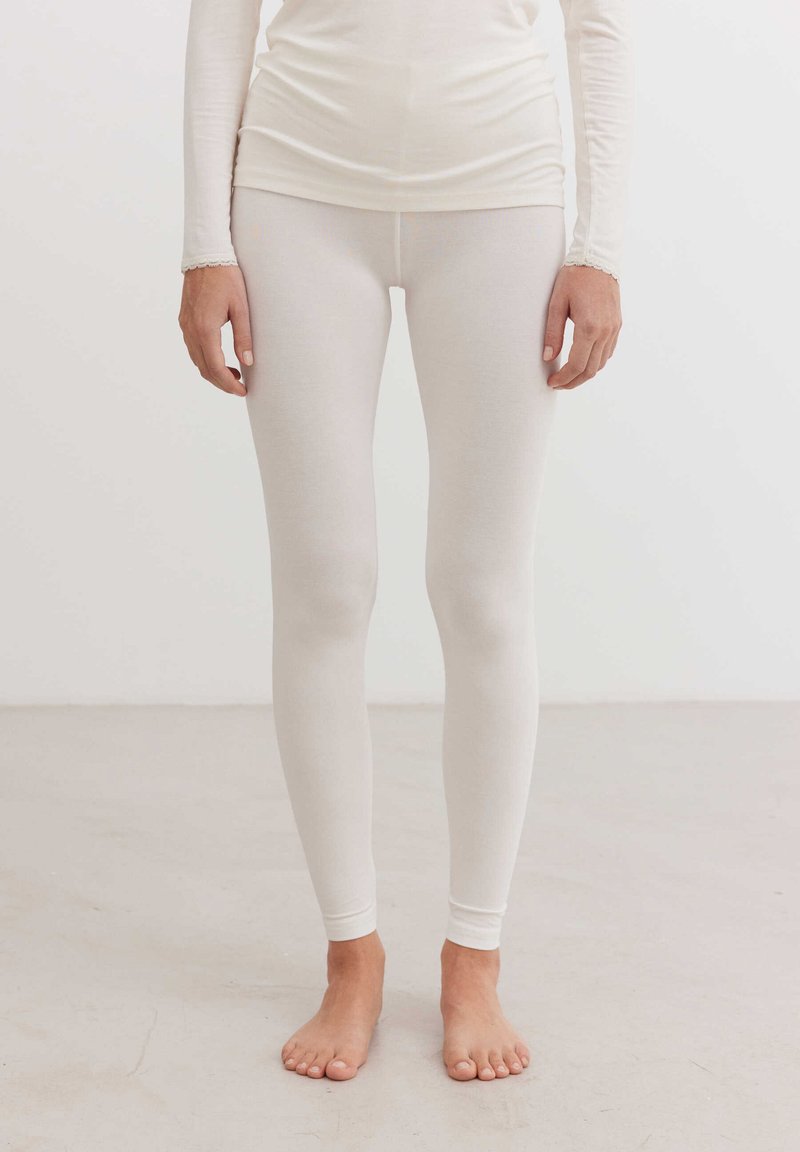 Fehér, testhezálló leggings puha, rugalmas anyagból. Sima felület ribbed derékpánttal és szoros mandzsettákkal a bokákon. Meztelen lábfejek láthatók.