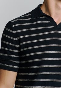 Zwart-wit gestreepte polo met een v-hals, korte mouwen en een textuurafwerking. De strepen zijn horizontaal en gelijkmatig verdeeld.