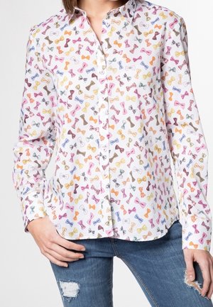White button-up shirt with colorful bow tie pattern worn with blue ripped jeans, shown from neck to hips.