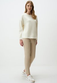 Pull en tricot crème avec un motif texturé, associé à un pantalon beige ajusté et des baskets blanches avec des accents beiges. Tenue simple et décontractée.
