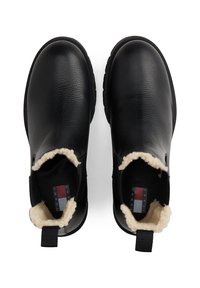Bottes noires en cuir à enfiler avec doublure en polaire beige et languettes, vues de dessus, affichant des étiquettes Tommy Jeans à l'intérieur.