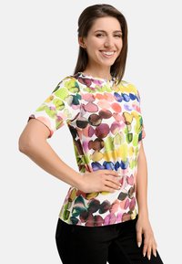 Short-sleeve, multicolored top featuring a watercolor flower pattern on a light background. Soft fabric with a round neckline and fitted shape.