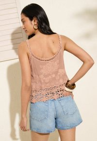 Top rosa chiaro con ricami floreali dettagliati e orlo in pizzo, abbinato a pantaloni shorts in denim azzurro chiaro. Tessuto liscio; spalline sottili.