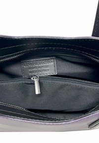 Interno di una borsa in pelle viola con fodera in tessuto nero, dotato di una tasca con zip e di un'etichetta che riporta la dicitura "Pelle Vera Fabbricata in Italia."