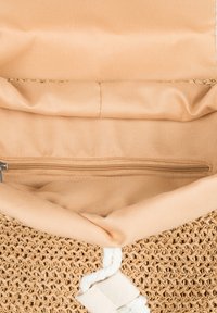 Woven straw handbag with a beige fabric lining. Features a zippered pocket inside and a twisted rope accent. Soft texture.