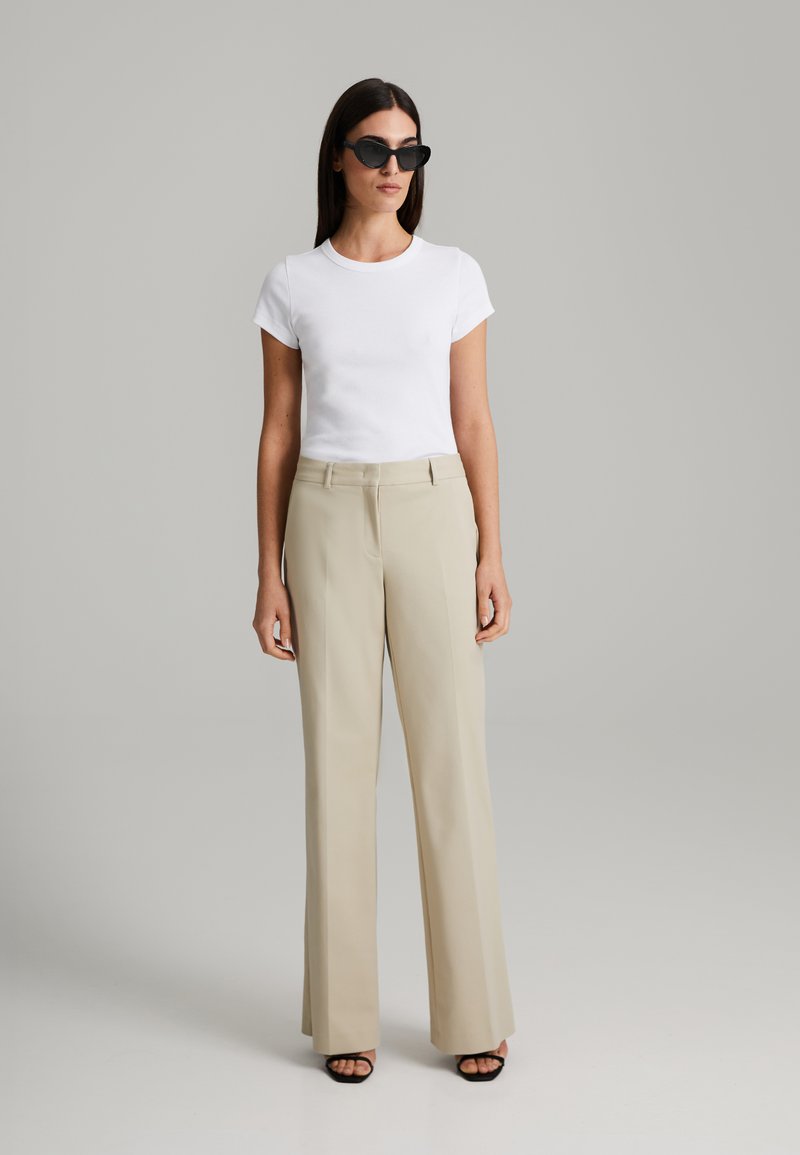White short-sleeve t-shirt paired with beige wide-leg trousers, featuring a smooth texture and a clean, minimalist design. Black sunglasses add contrast.