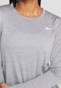 Närbild av en person som bär en grå långärmad Nike-tröja med den vita swoosh-logotypen på höger bröst.