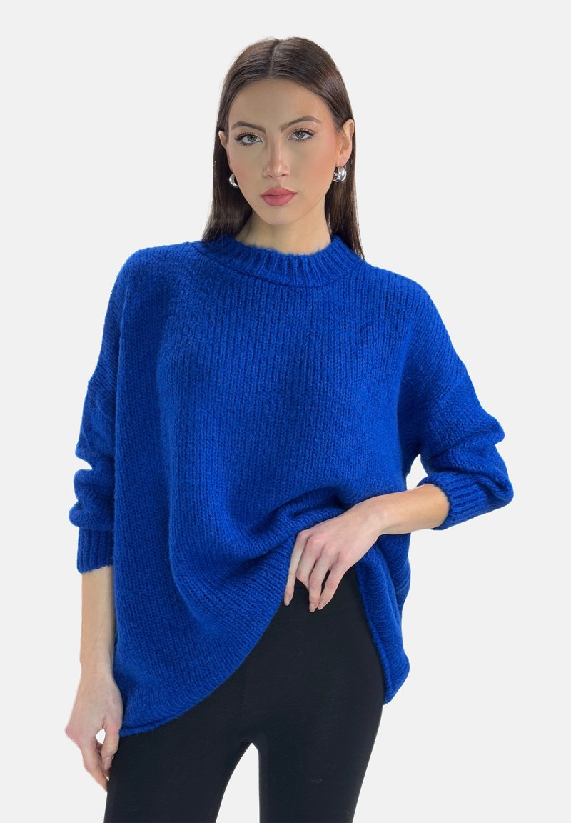 Maglione blu oversize in maglia con texture a costine, colletto alto e maniche arrotolate, abbinato a pantaloni neri aderenti.