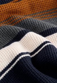 Couverture en tricot avec des rayures orange, gris, marine et crème. Tissu texturé avec un motif gaufré, apparence douce et confortable.