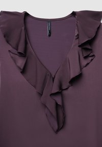 Blusa viola con scollo a V e accenti arricciati lungo il bordo. Tessuto morbido con una consistenza liscia e un dettaglio centrale con bottone.