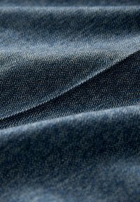 Close-up of dark blue fabric with a herringbone pattern and soft folds creating shadows and texture.