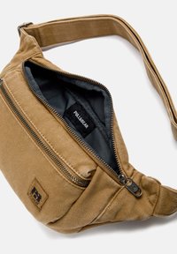 Borsa in tessuto color sabbia con scomparto principale con zip, fodera nera, tasca frontale con zip e una toppa con logo. Include una tracolla regolabile.