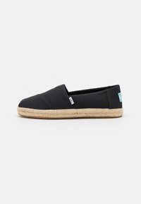 Scarpa slip-on nera in tela con superficie testurizzata, suola in juta naturale intrecciata e piccolo etichetta logo blu e bianca sul lato.