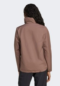 Veste imperméable marron avec un col haut, des manches longues et des poignets élastiques. Texture lisse conçue pour une utilisation en extérieur.