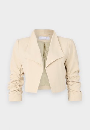 Beige croppete jakke med overdimensjonert krage, rynkede ermer og en glatt tekstur. Innerforet har en kontrasterende lys grønn farge.