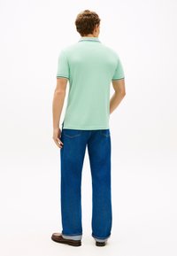 Μπλούζα πόλο μέντας με κοντράστ γιακά και λεπτομέρειες στα μανίκια, συνδυασμένη με ψηλόμεσο τζιν μπλε. Λείο ύφασμα και άνετη εφαρμογή.
