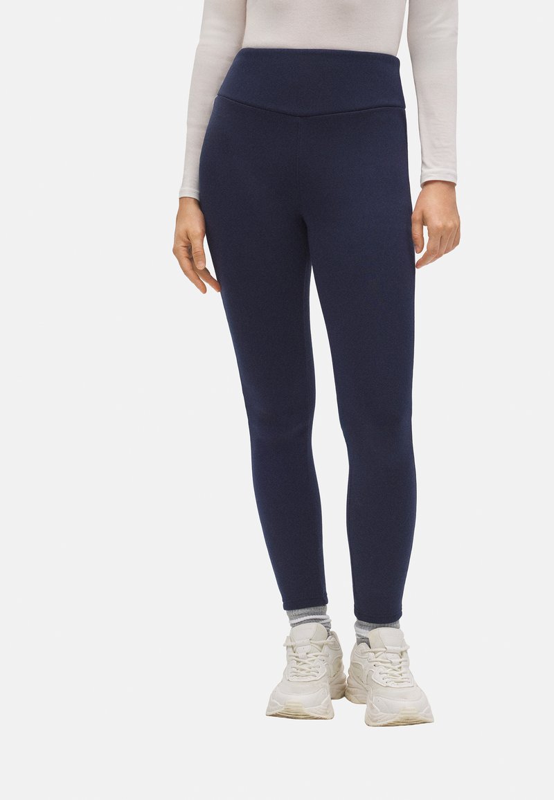 Leggings azul marino con cintura alta, hechos de material elástico, con una textura suave y un diseño ajustado. Combinados con zapatillas blancas.