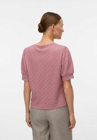 Roze textuur blouse met korte pofmouwen en een ronde halslijn, gecombineerd met lichtgrijze broek. Heeft een geweven patroon.