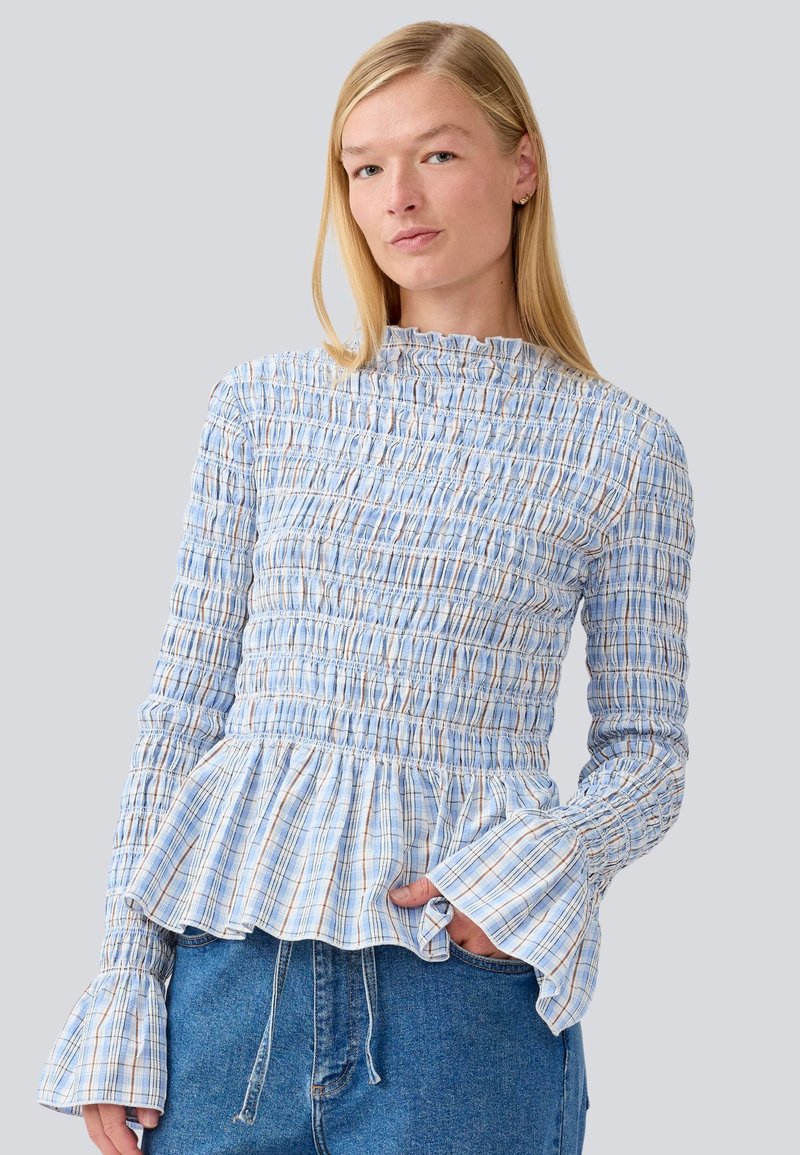 Blusa quadriculada azul e branca com textura franzida, gola alta e mangas largas; detalhe de bainha peplum; feita de tecido leve.