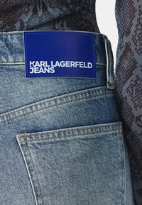 Blauwe denim jeans met een zichtbare achterzak en een blauwe label genaaid in de tailleband met de tekst "KARL LAGERFELD JEANS" in witte letters.