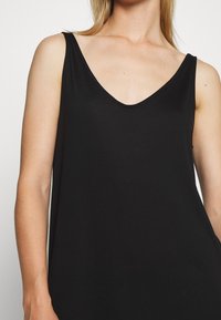 Schwarzes ärmelloses Top mit einem V-Ausschnitt, aus glattem Stoff gefertigt, der die Schultern und das Dekolleté betont. Einfacher und minimalistischer Look.