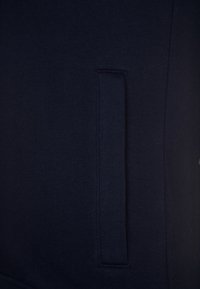 Tissu bleu marine foncé avec une poche fendue verticale présentant des coutures propres et renforcées le long des bords.