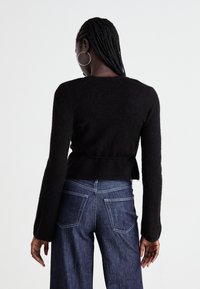 Svart genser laget av strukturert strikk, med lange ermer og cropped hem, kombinert med mørkeblå høyhøyde jeans.