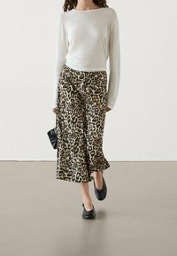 Leichtes, weißes Langarmoberteil, kombiniert mit weiten Hosen im braun-schwarzen Leopardenmuster. Schwarze Flatschuhe und eine schwarze Clutch.
