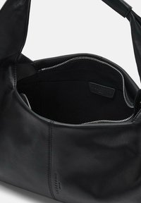 Czarna skórzana torba o miękkim, zaokrąglonym kształcie. Wnętrze ma zamek błyskawiczny i gładką podszewkę tekstylną, z subtelnym logo widocznym w środku.